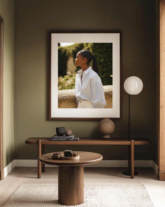 Framed portrait of a woman on a wall above a wooden table in a hallway with olive green walls.