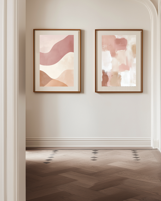 Two abstract pink and beige art pieces in wooden frames on a wall with a wooden floor.