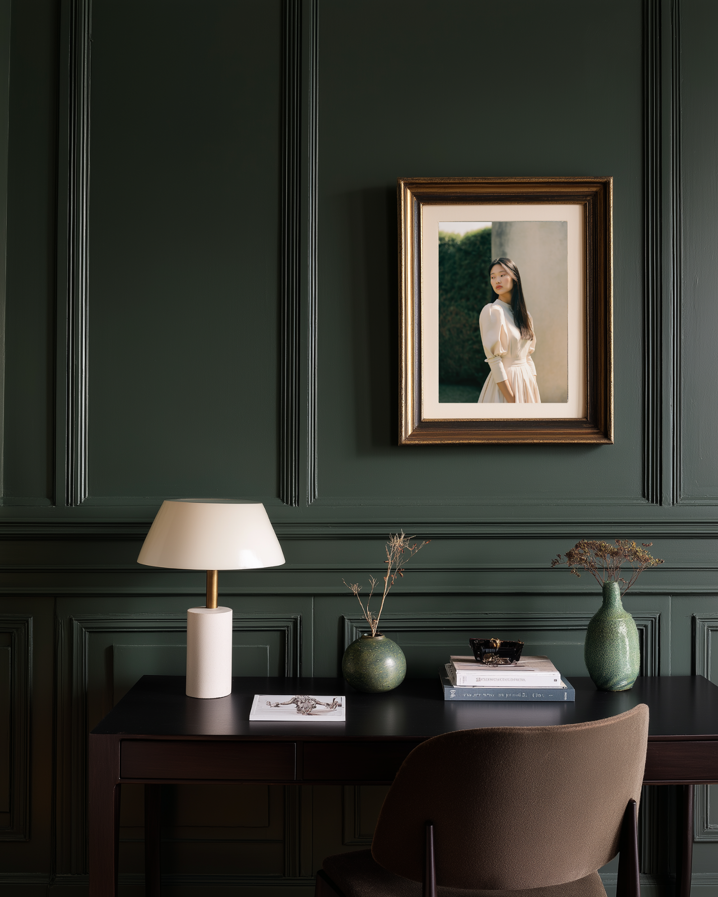 Dark green wall with framed portrait, desk with lamp and decor items.