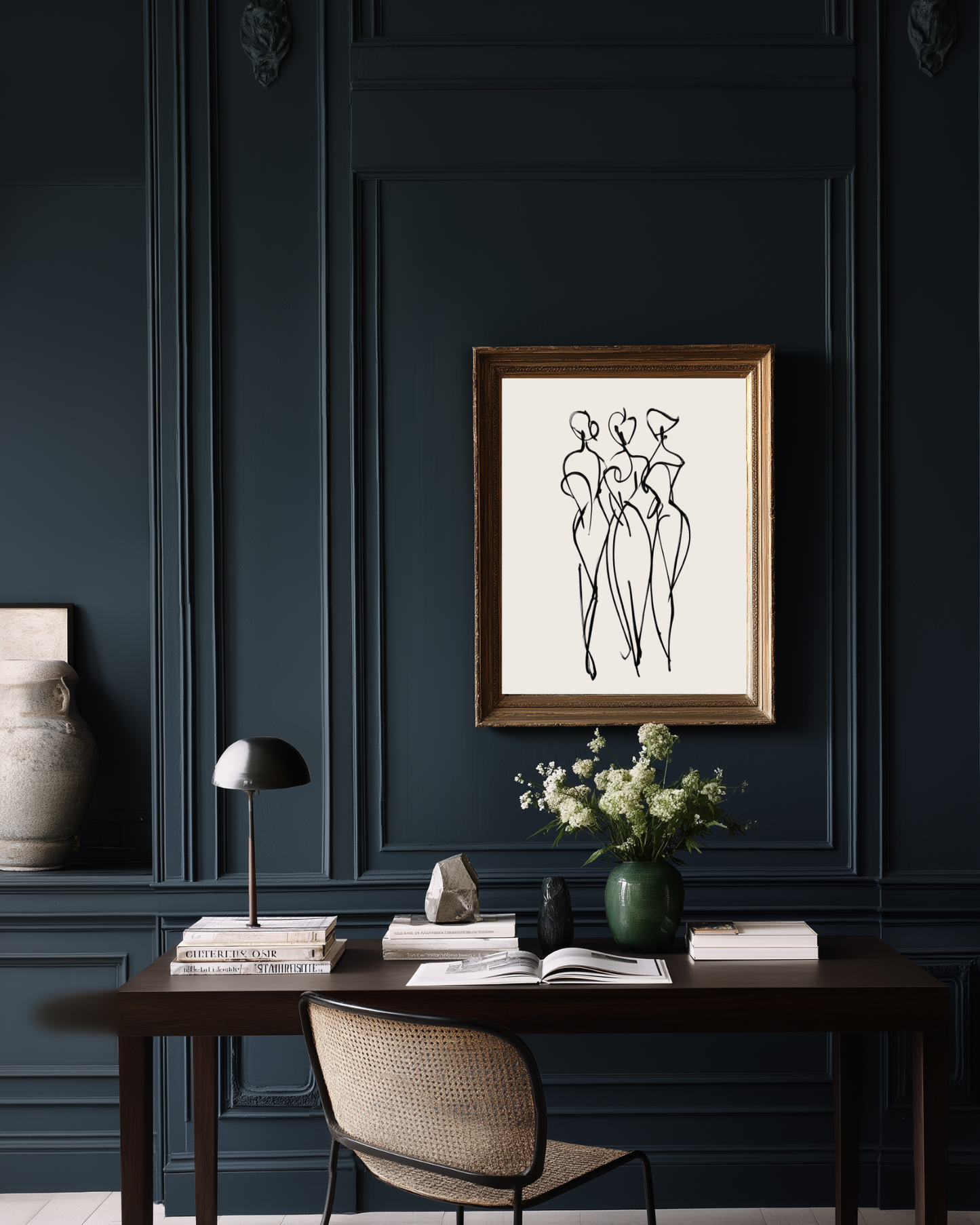 Framed abstract women minimalist wall art on a dark blue wall above a desk with decor items.