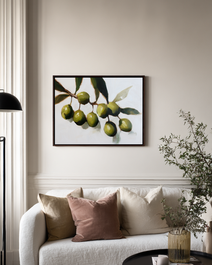 Framed artwork of green olives on a wall above a sofa with decorative pillows.