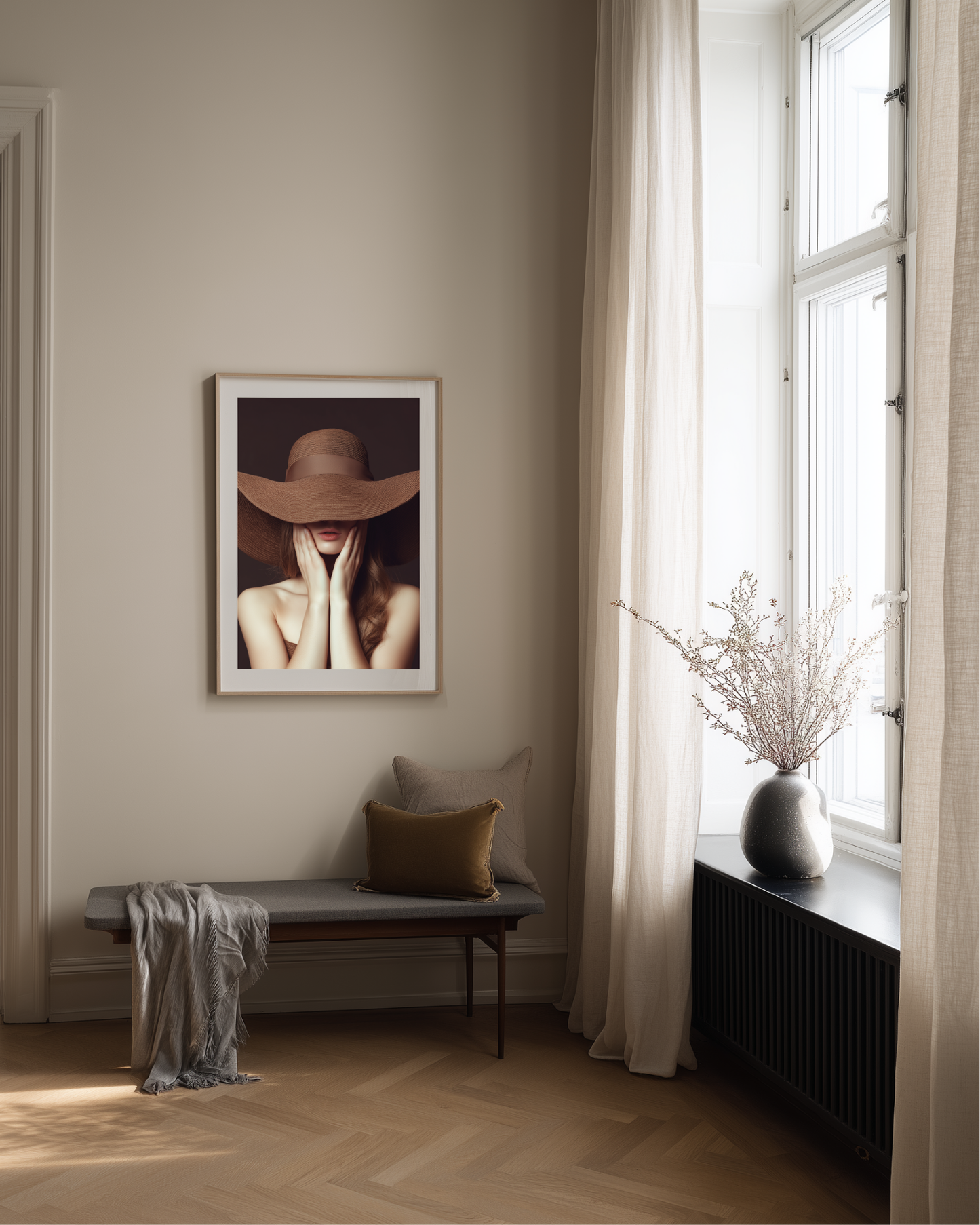 Room interior with a framed fashion photography art print of a woman wearing a brown hat, a bench with a pillow and blanket, and a window with white curtains.