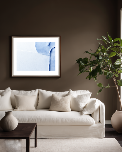 Living room with a white sofa, abstract light blue art on the wall, and a plant.