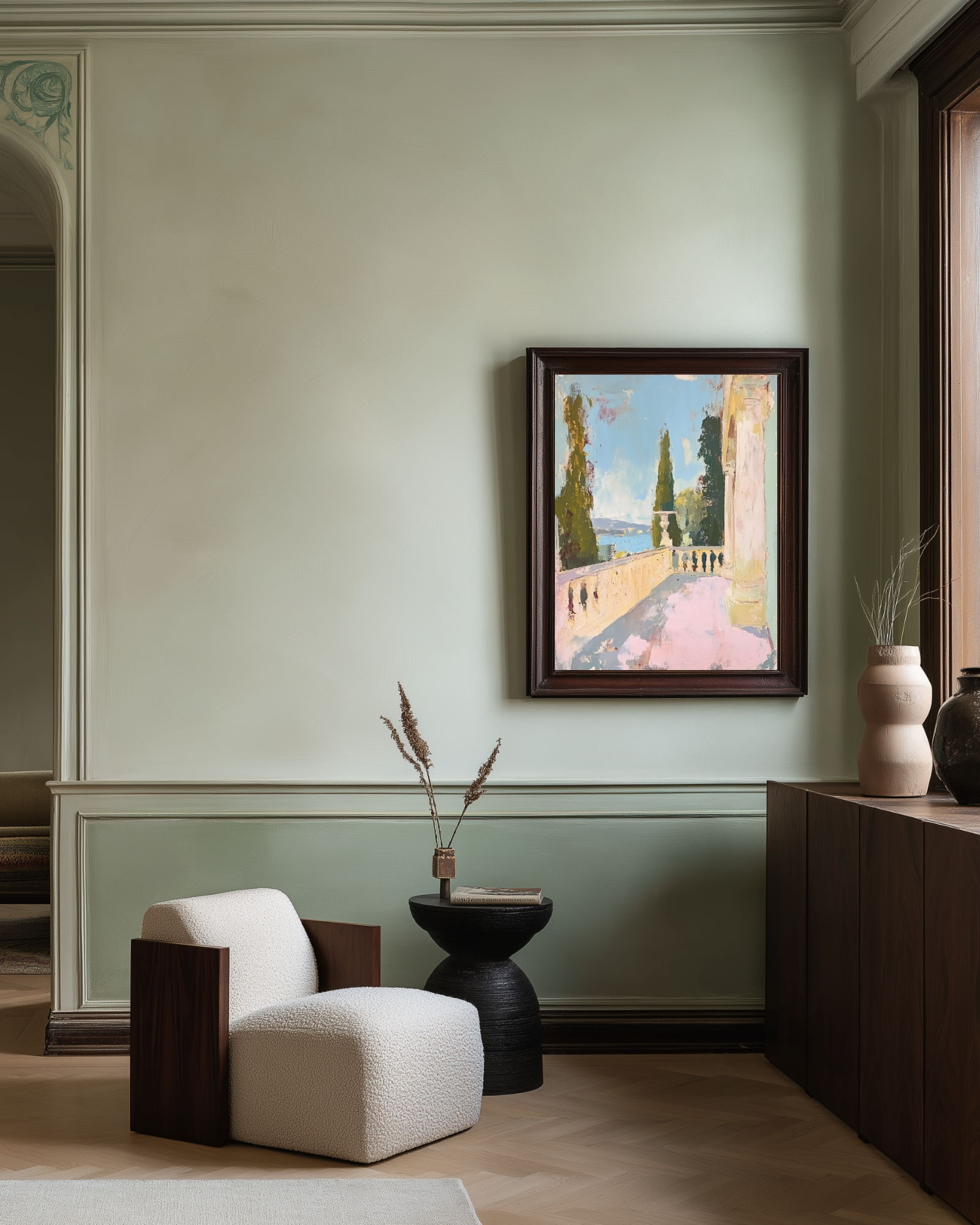 Modern interior with a white armchair, black side table, and framed pastel artwork on a light green wall.