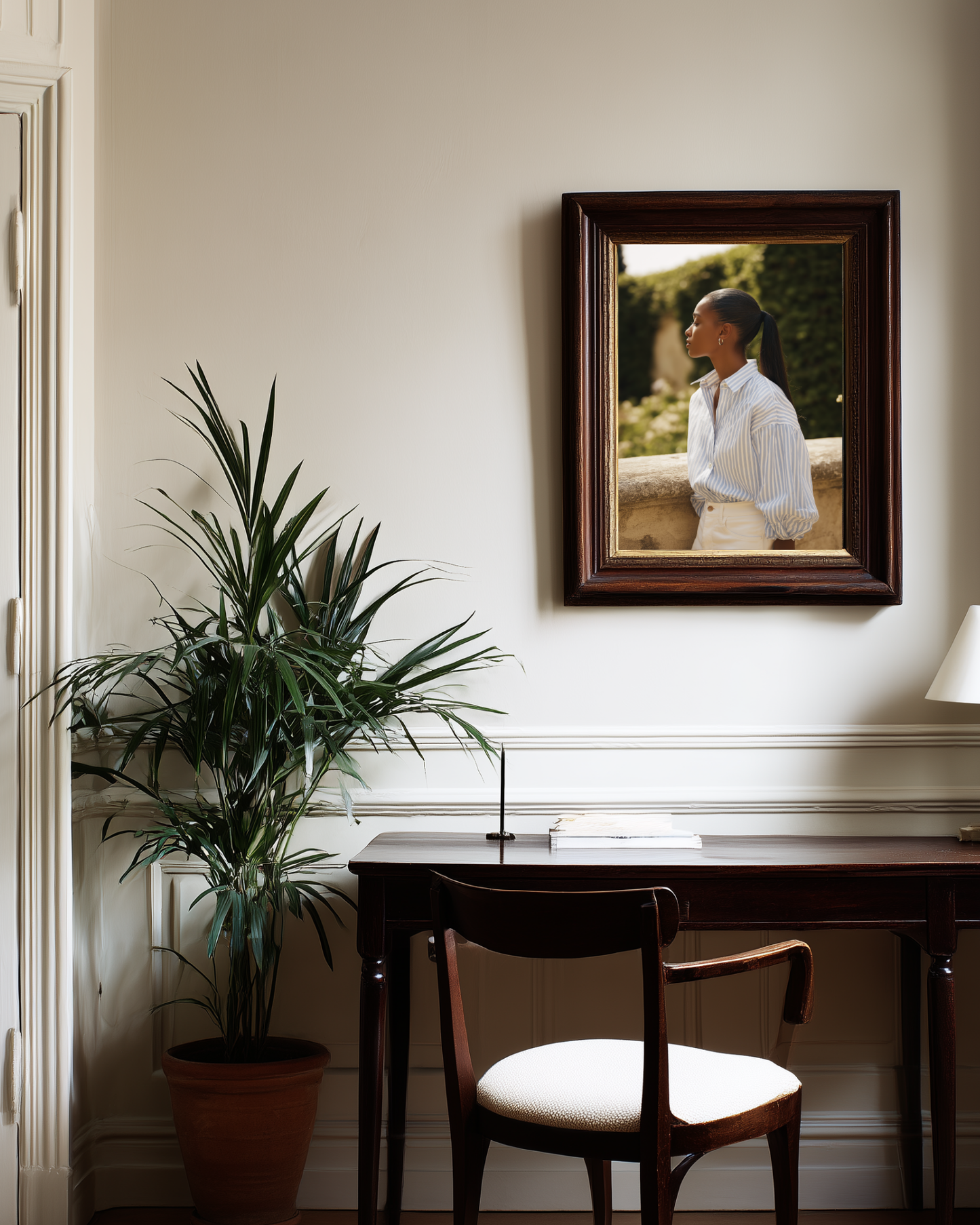 Room interior with a desk, chair, potted plant, and framed fashion poster on the wall.