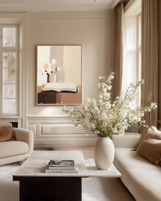 Living room with a vase of white flowers on a coffee table, beige walls and a framed painting with an open book