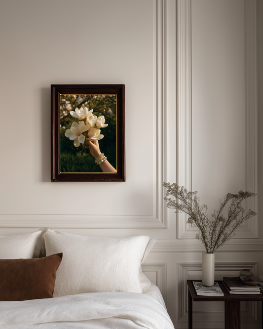 Framed artwork of a hand holding flowers on a wall above a bed.